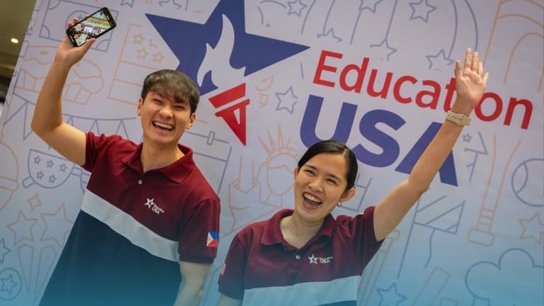 EducationUSA staff cheering in front of the fair backdrop
